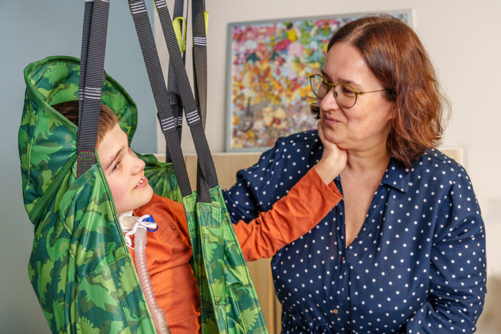 A young boy in a camo pediatric sling with his mother