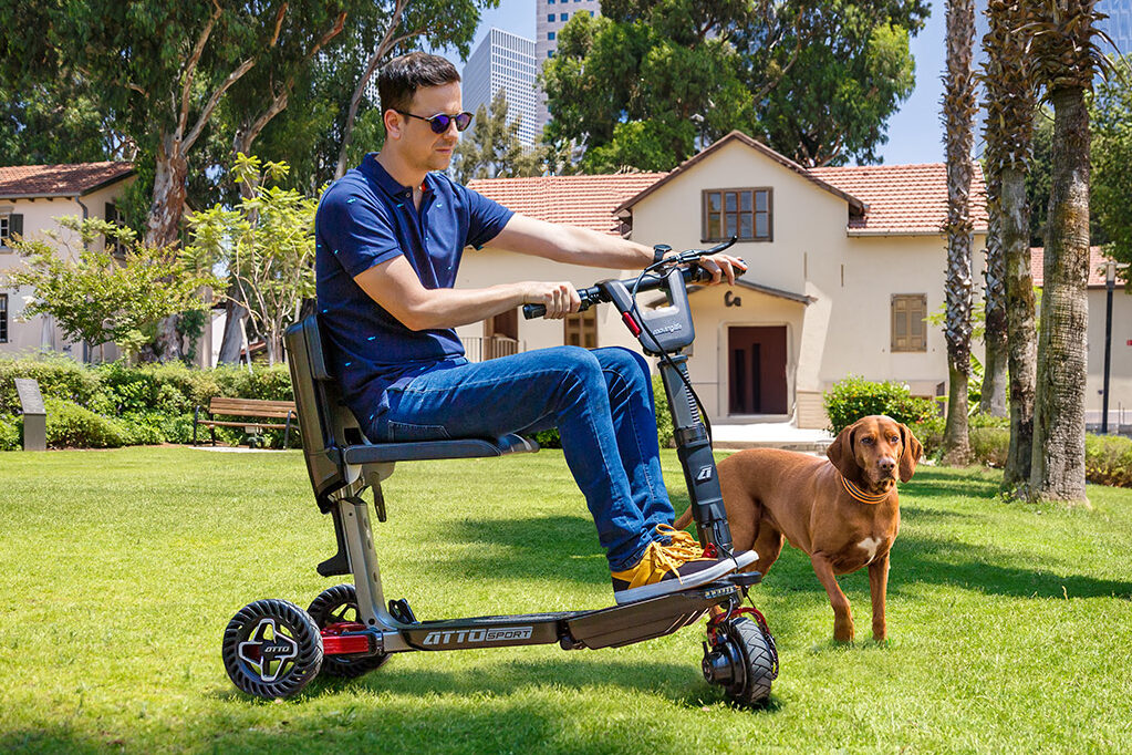 A man is riding a Movinglife ATTO Sport around his spacious front yard with his dog.