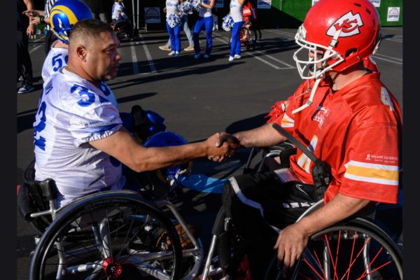 A wheelchair football player wearing an LA Rams Jersey shaking the hand of a wheelchair football player wearing a Kansas City Chiefs uniform and helmet.
