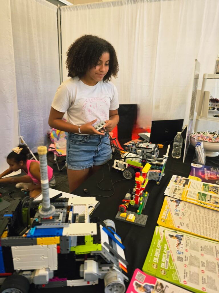 A girl stands opperating her robotic creation, amidst a group of other robotic creations.