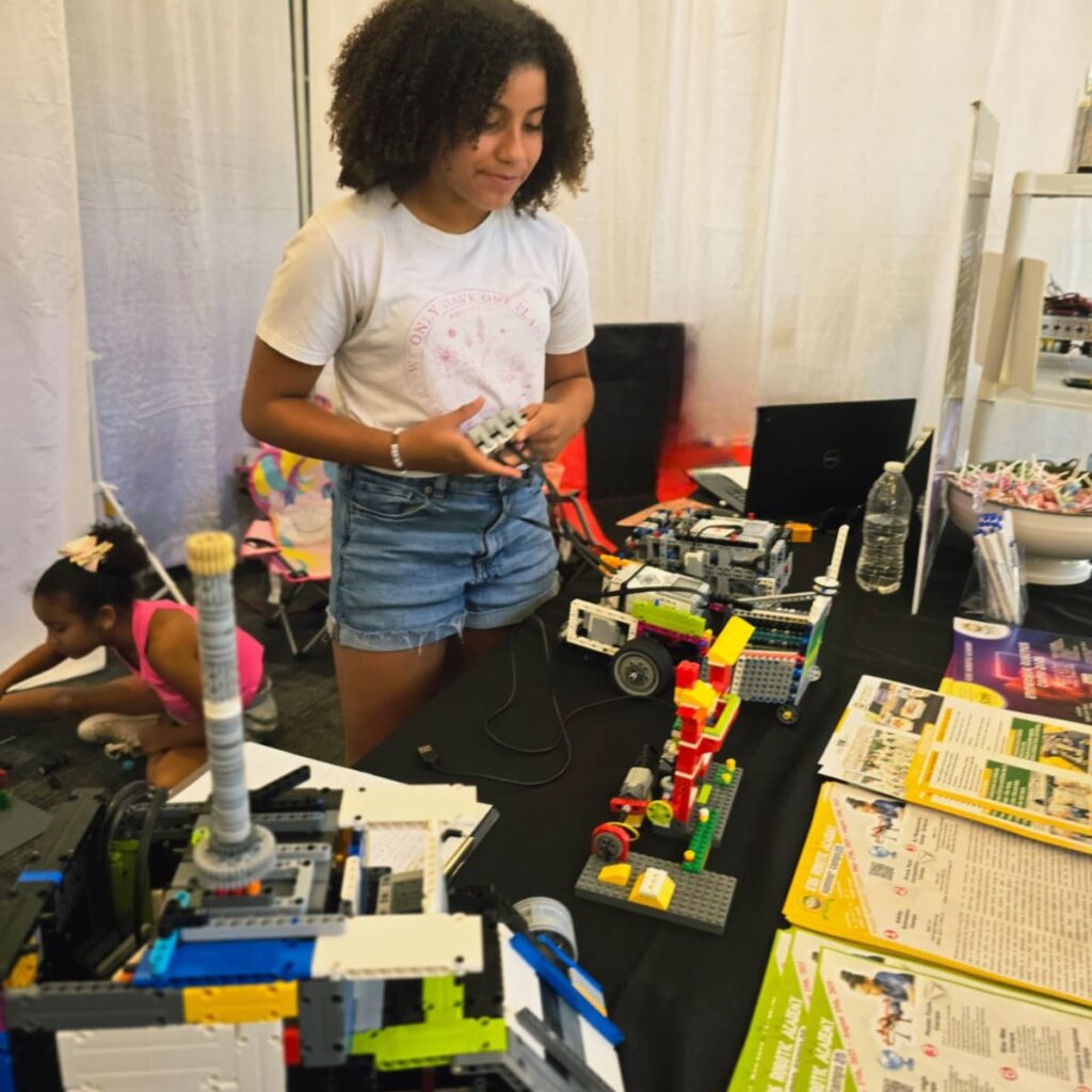A girl stands opperating her robotic creation, amidst a group of other robotic creations.