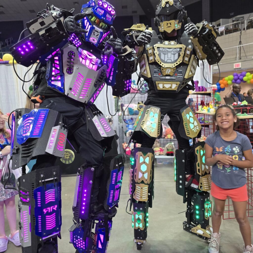 Two giant purple and silver Robot Stilt Walkers tower of a little kid as they pose for a picture.