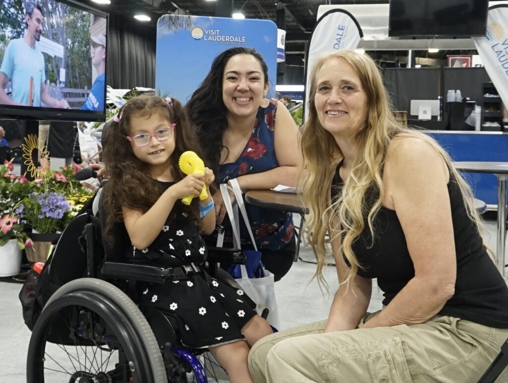 Two women and a young girl in a wheelchair lounge in the Visit Lauderdale Beach Cafe.