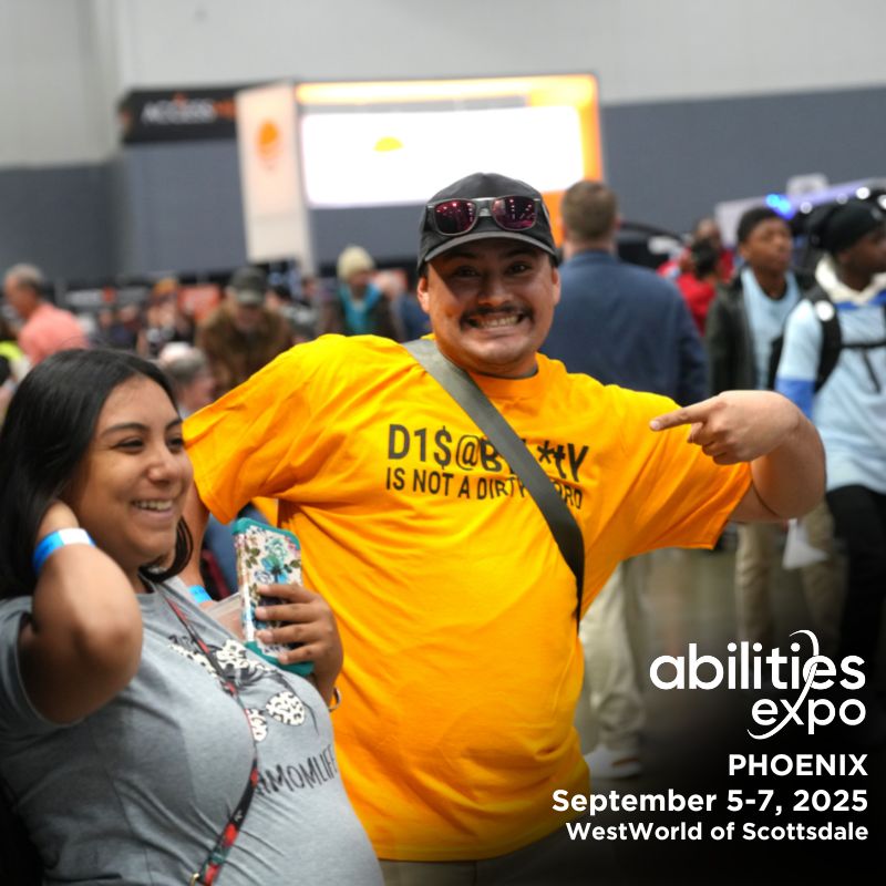 A happy couple is enjoying their time on the show floor of Abilities Expo. The man points at his t-shirt which reads: Disability is not a dirty word. It reads: 'abilities expo, Phoenix, September 5-7, 2025, WestWorld of Scottsdale.