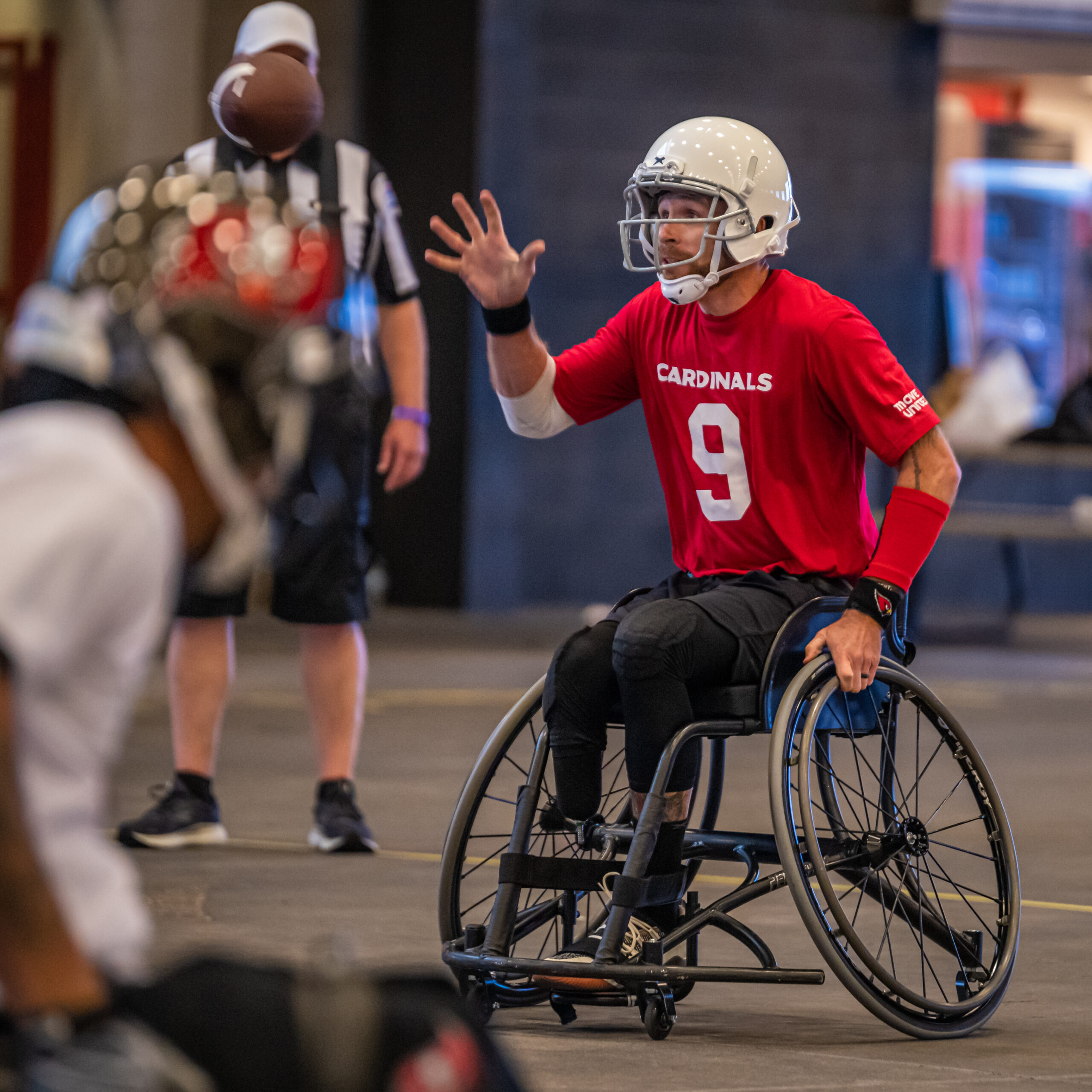 Adaptive football player wearing a read Cardinals jersey holding his hand up.
