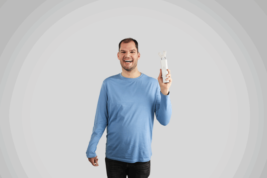 A man in a blue shirt smiling and holding up the Samba robotic toothbrush.