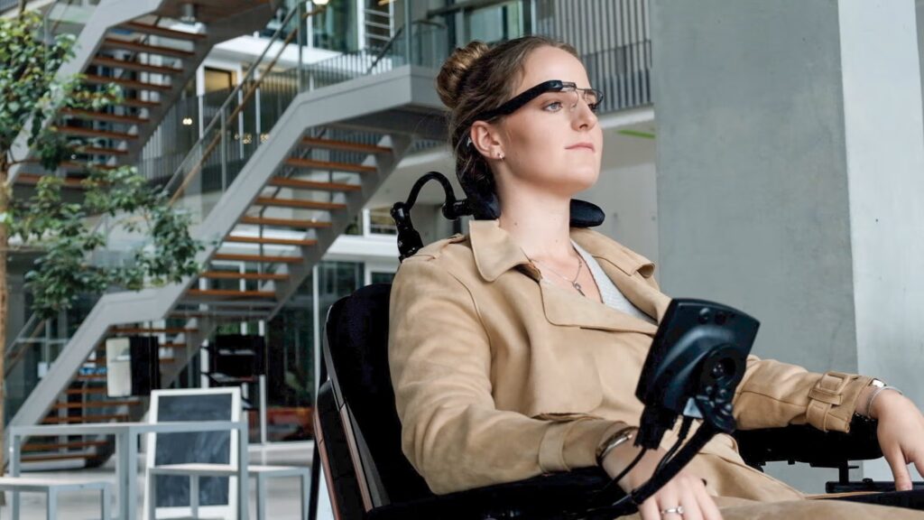 A woman is driving her power chair with munevo drive controls which are attached to the glasses.