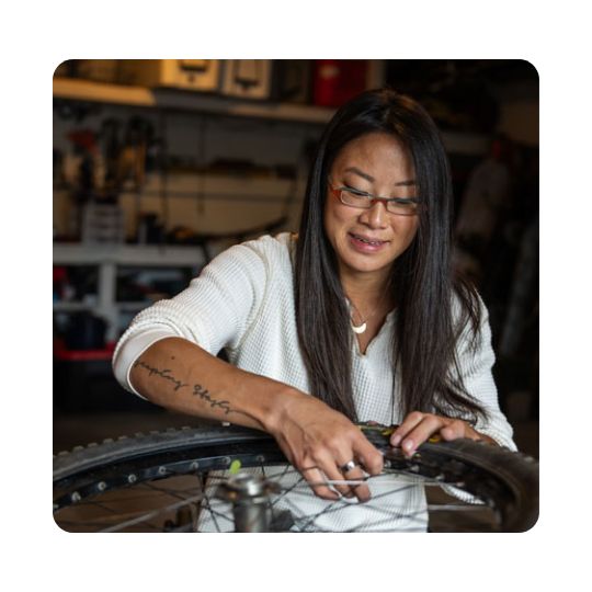 A woman in glasses fixes the wheel of a wheelchair
