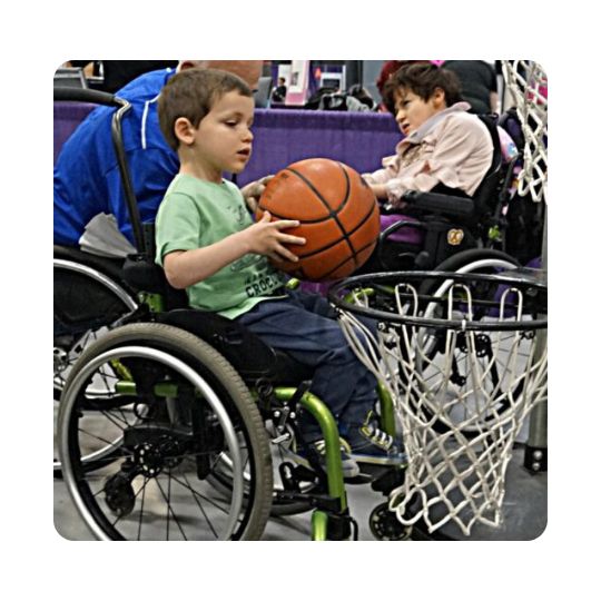 A young boy in a wheelchair is playing wheelchair basketball