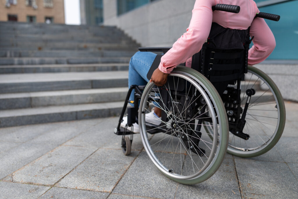 Unrecognizable young black paraplegic woman in wheelchair cannot go up stairs without ramp, feeling limited and unhappy, cropped.