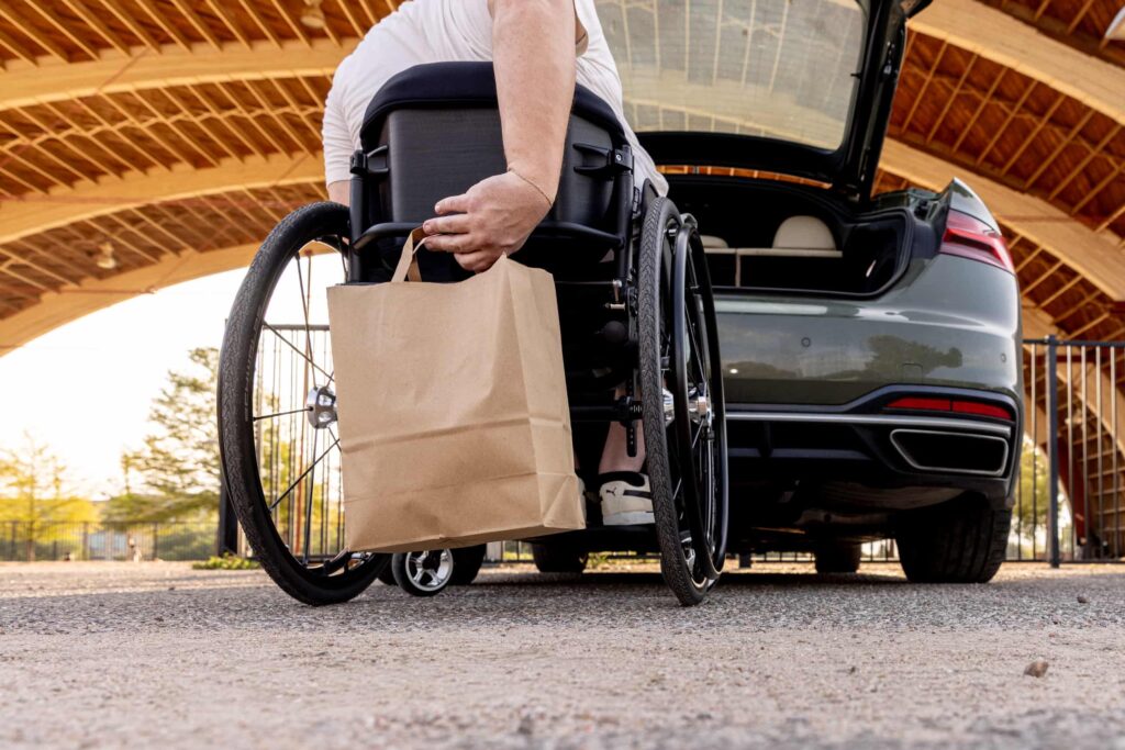 A man uses the make easy hang in order to hang his grocery bag on the bag of his wheelchair.