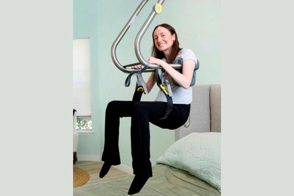 A smiling woman is suspended over her bed in a Surehand lift.