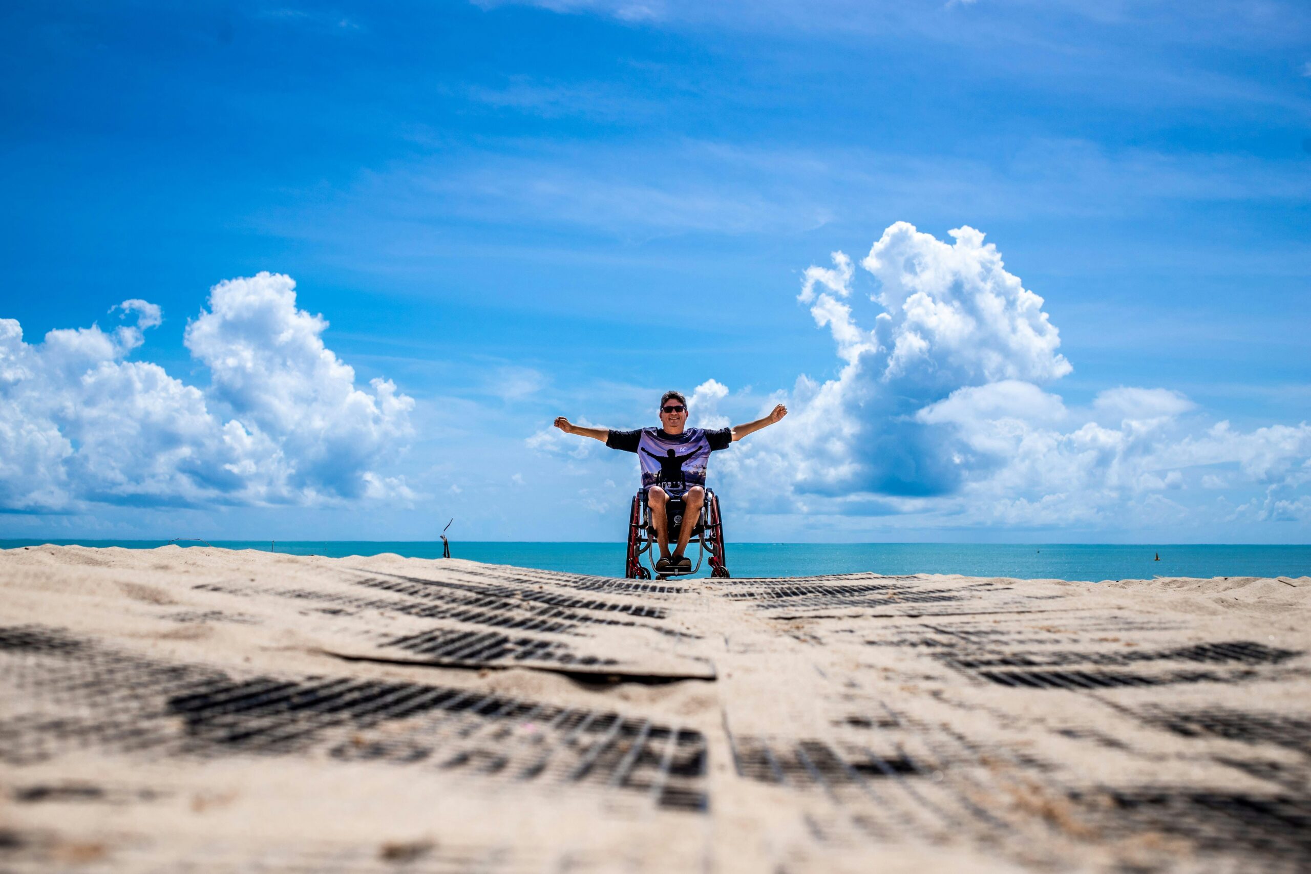 Man using a wheelchair poses for the camera on the beach