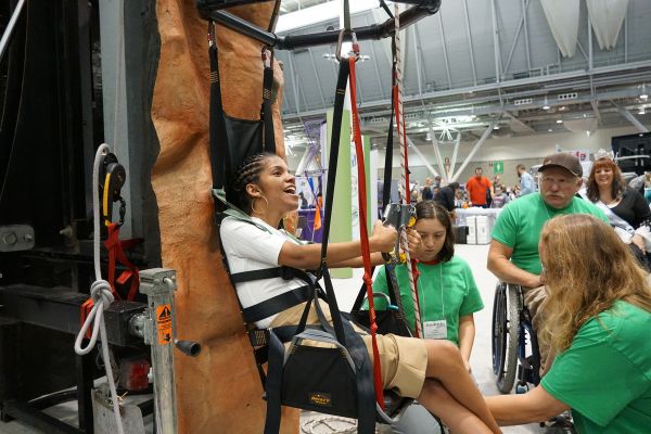 A young woman scales the Abilities Expo adaptive climbing wall.
