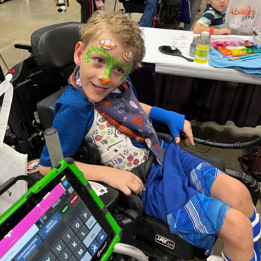 A little boy in a wheelchair is happily sporting his new face paint.