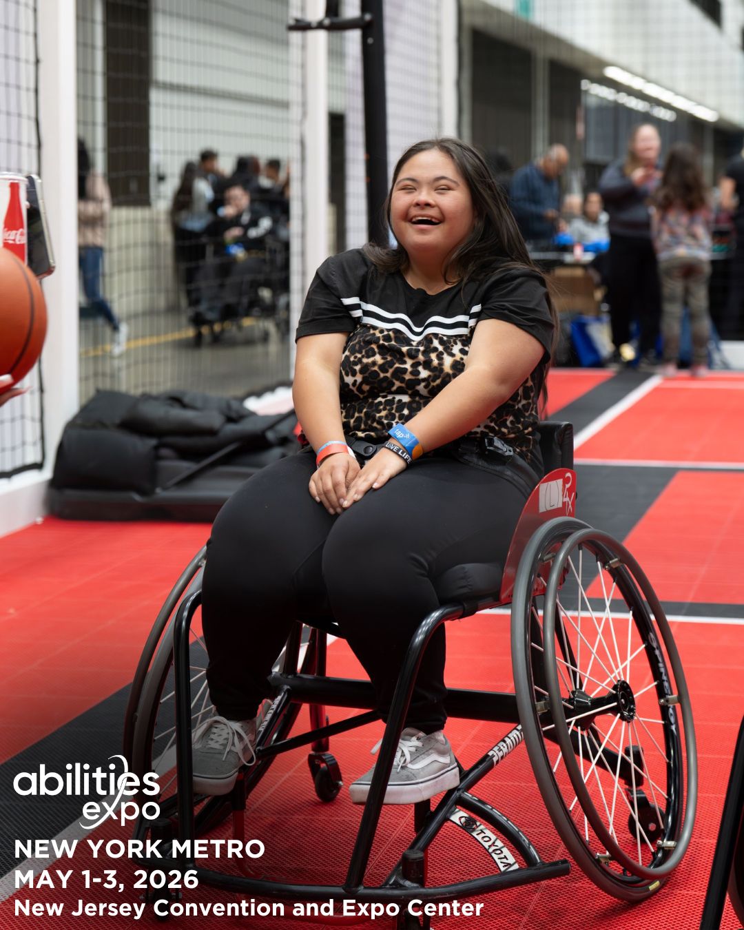 A young girl in a wheelchair is smiling on an adaptive basketball court