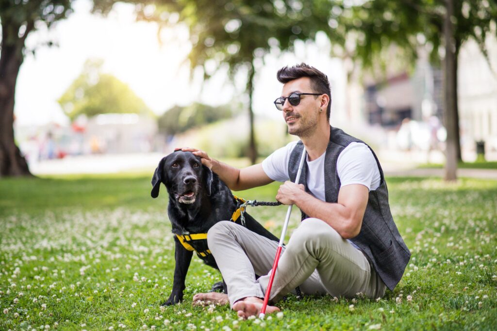 A blind man lounges on a lawn with his dog