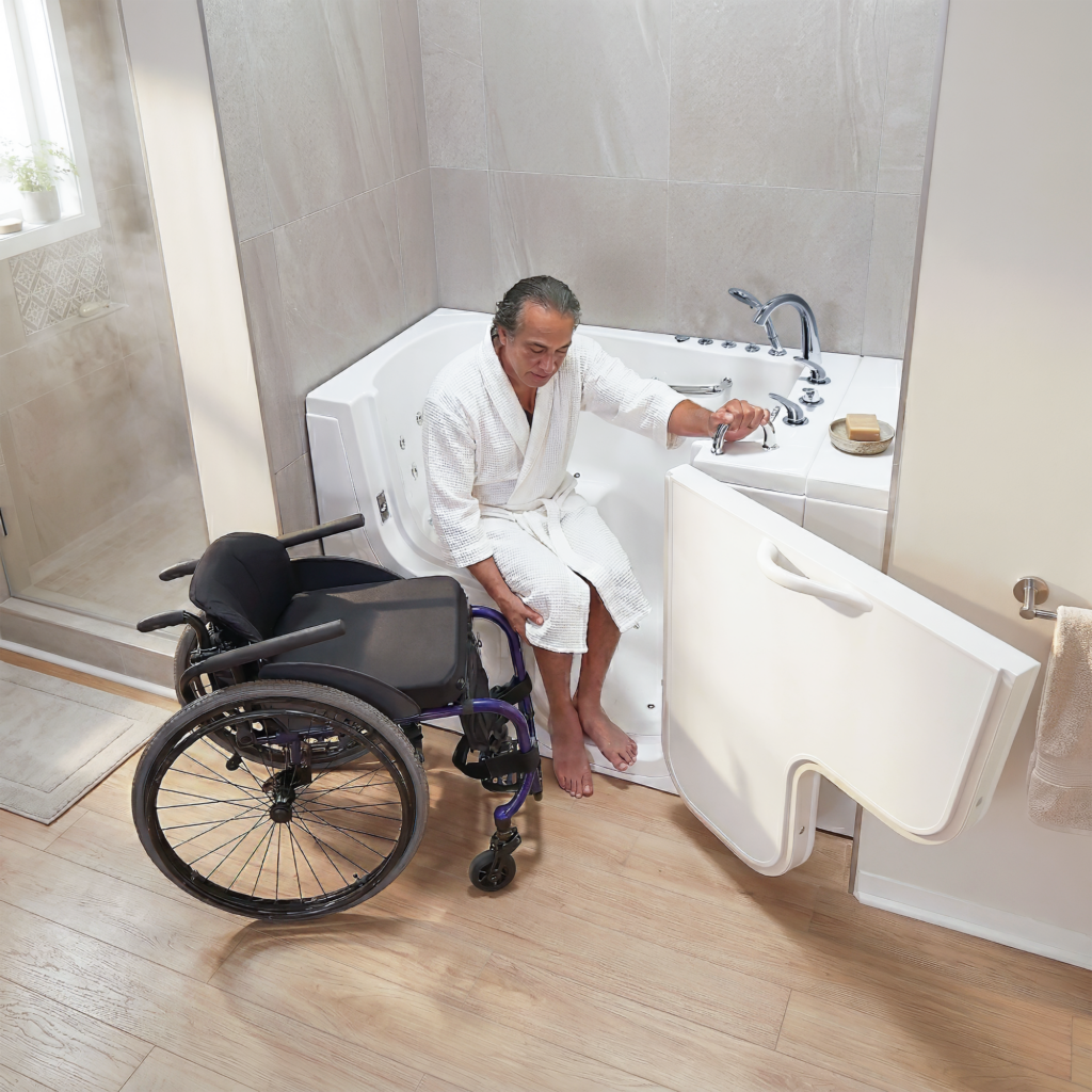 Man transferring from a wheelchair into an Ella’s Bubbles accessible walk-in tub with outward-swing transfer door in a modern bathroom.