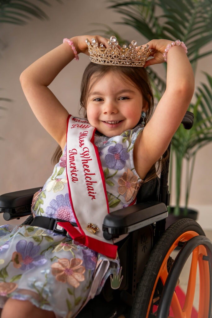 Little Miss Wheelchair America, Dahlia Swanson, smiling andposing in a dress, crown, and Little Miss Wheelchair sash.