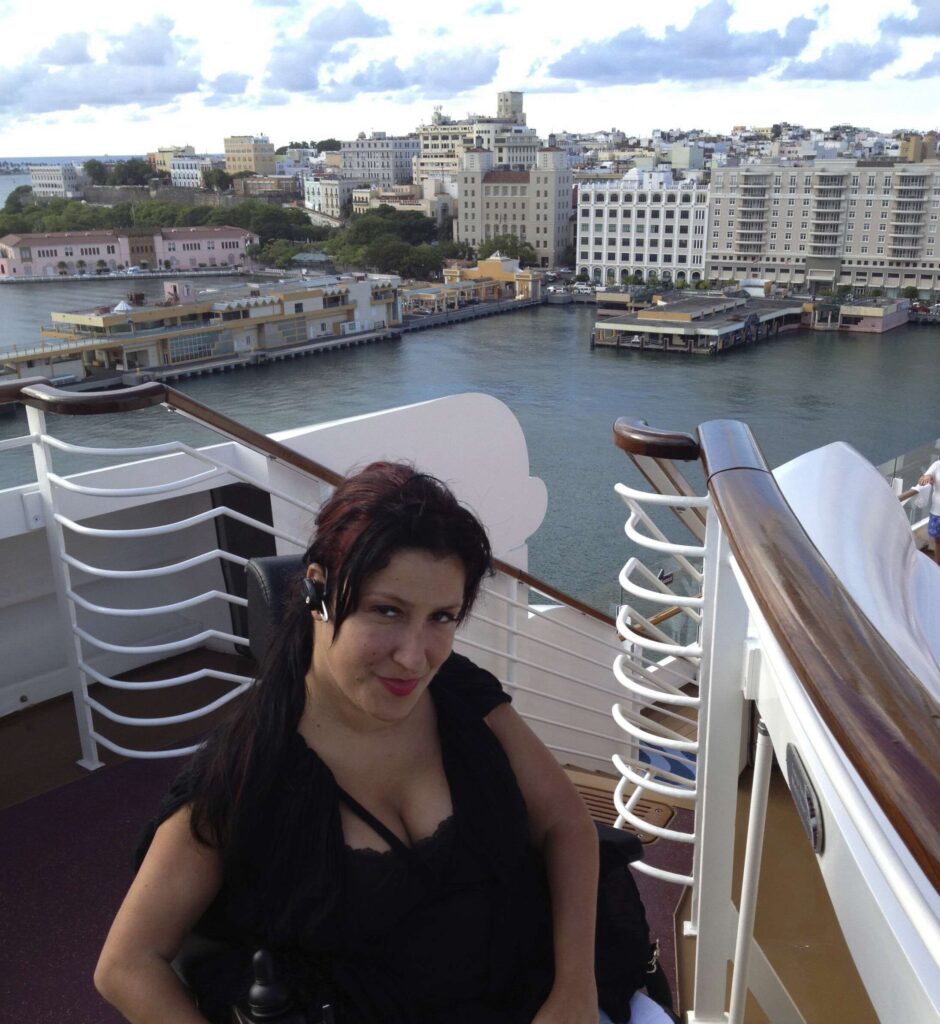 A photo of Yolanda Vicente smiling on the upper deck of a cruise ship with a city in the background