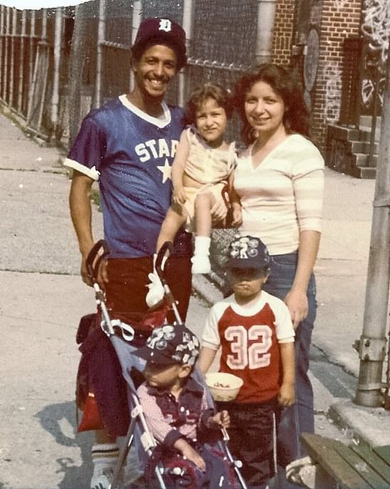 A photo of Yolanda Vicente as a young girl with her family. She is carried by her mother and father, with her two younger brothers below them. One brother is standing and the other is in a stroller.