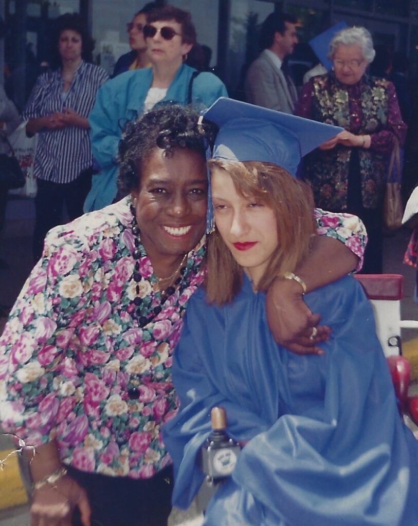 A photo of Yolanda Vicente in her high school graduation robes. She is being hugged by a woman in a pink floral shirt