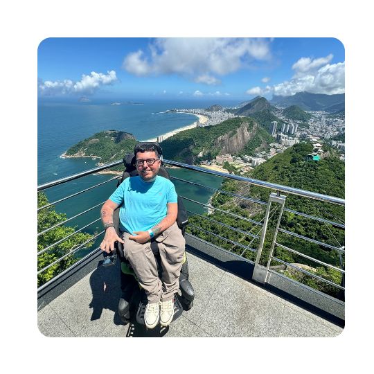 Cory Lee smiling for a photo by a fenced-off ledge overlooking a scenic landscape of Brazil