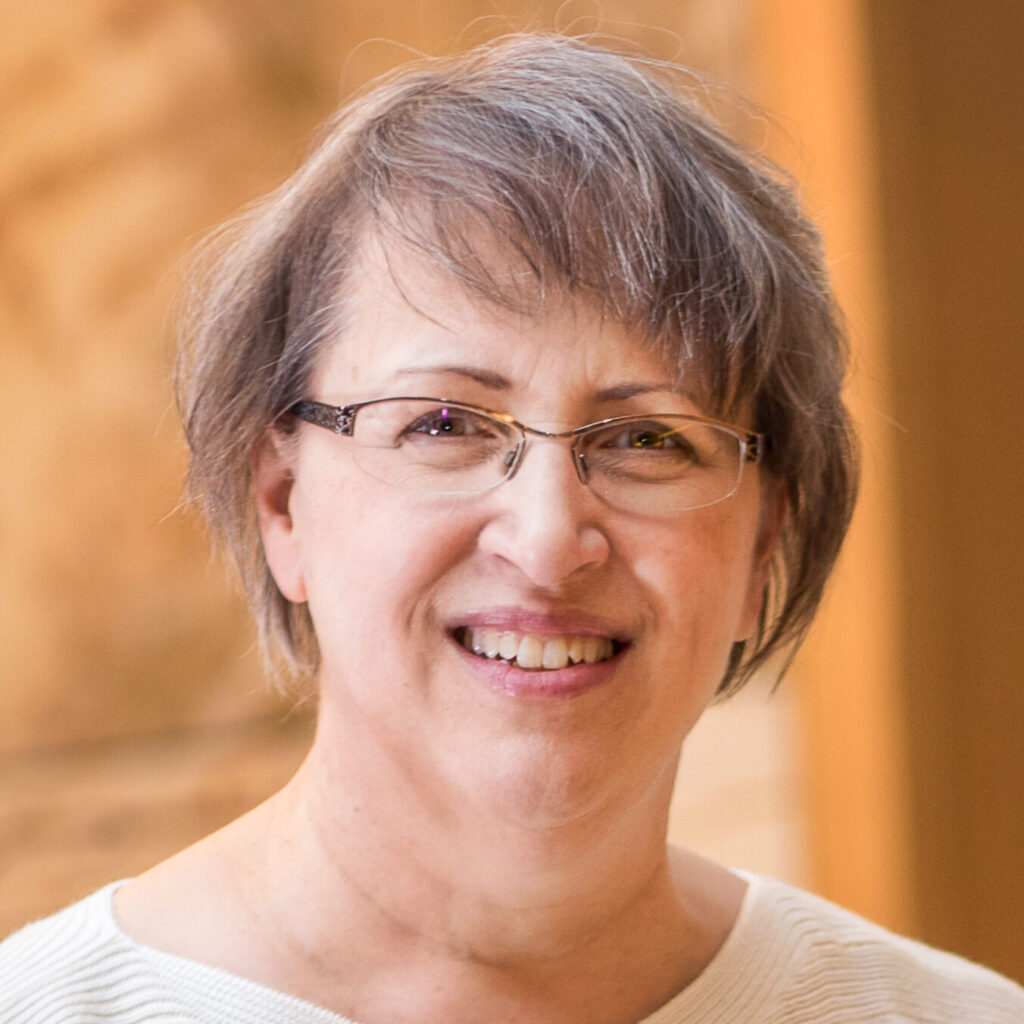 Headshot of Cindy Kolbe, smiling at camera wearing glasses and a white blouse