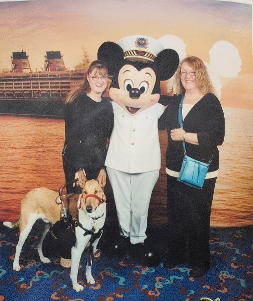 Two woman, a service dog and Cruise Captain Mickey Mouse all pose together for a photo