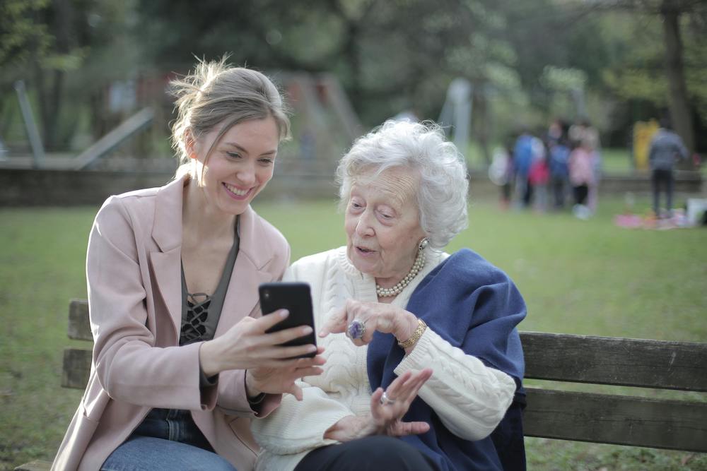 a young woman looks at a phone with an elderly woman